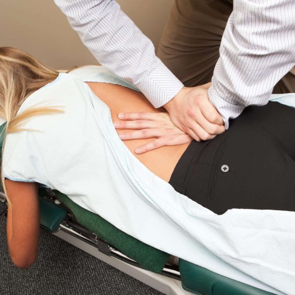 A male chiropractor is adjusting a woman's lower spine. The patient is on a specialized high/low chiropractic table.