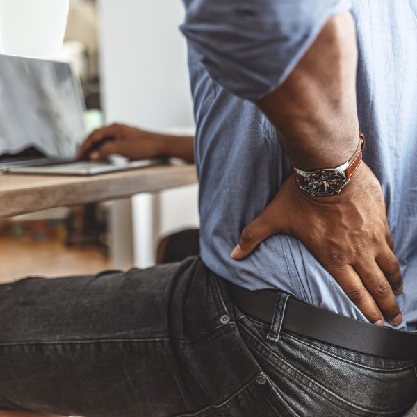 Businessman working sitting at desk feels unhealthy suffers from lower back pain. Damage of intervertebral discs, spinal joints, compression of nerve roots caused by wrong posture and sedentary work.